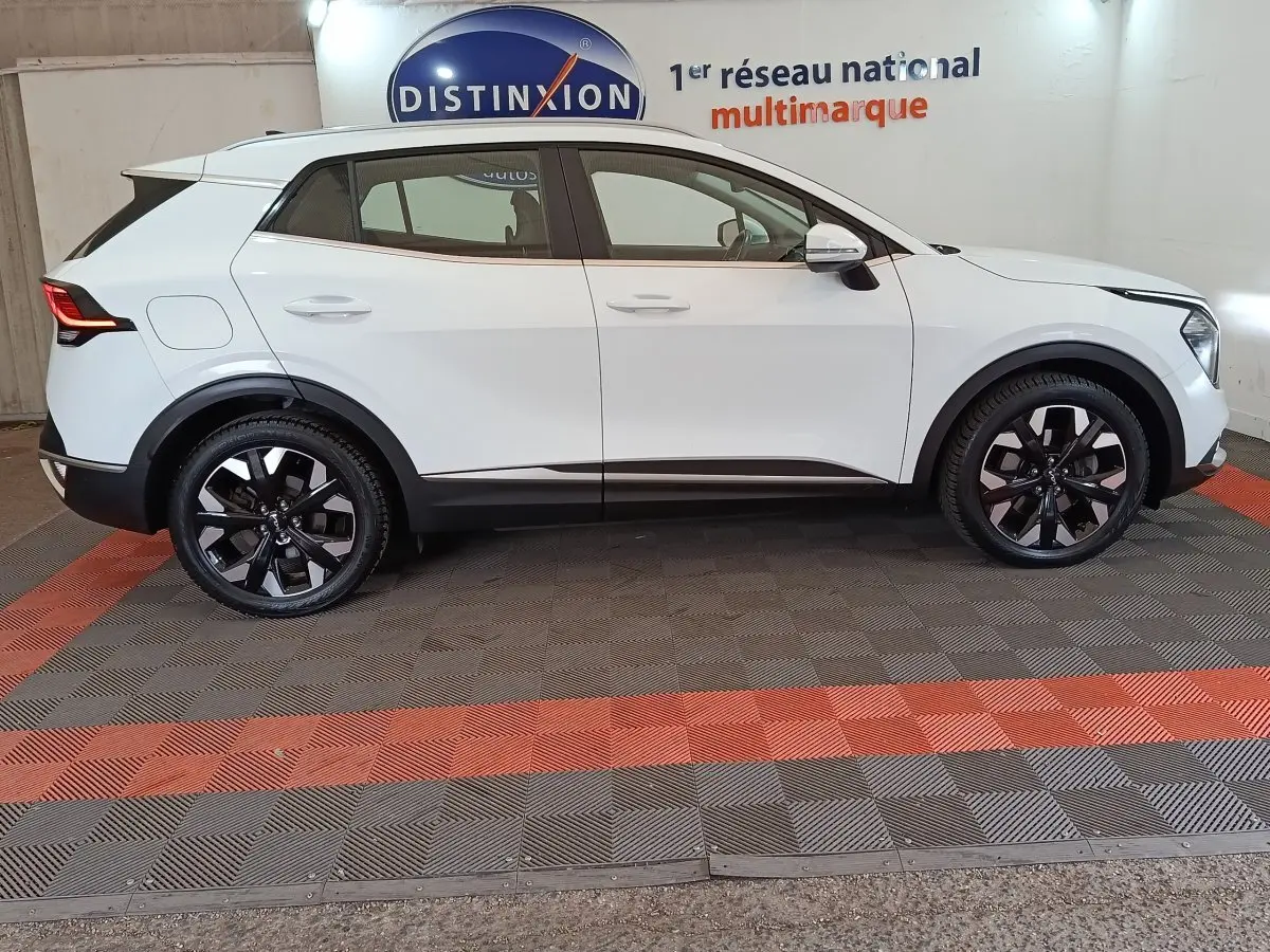Vue profil côté gauche d’un Kia Sportage blanc 2022 hybride rechargeable avec jantes noires et toit blanc.