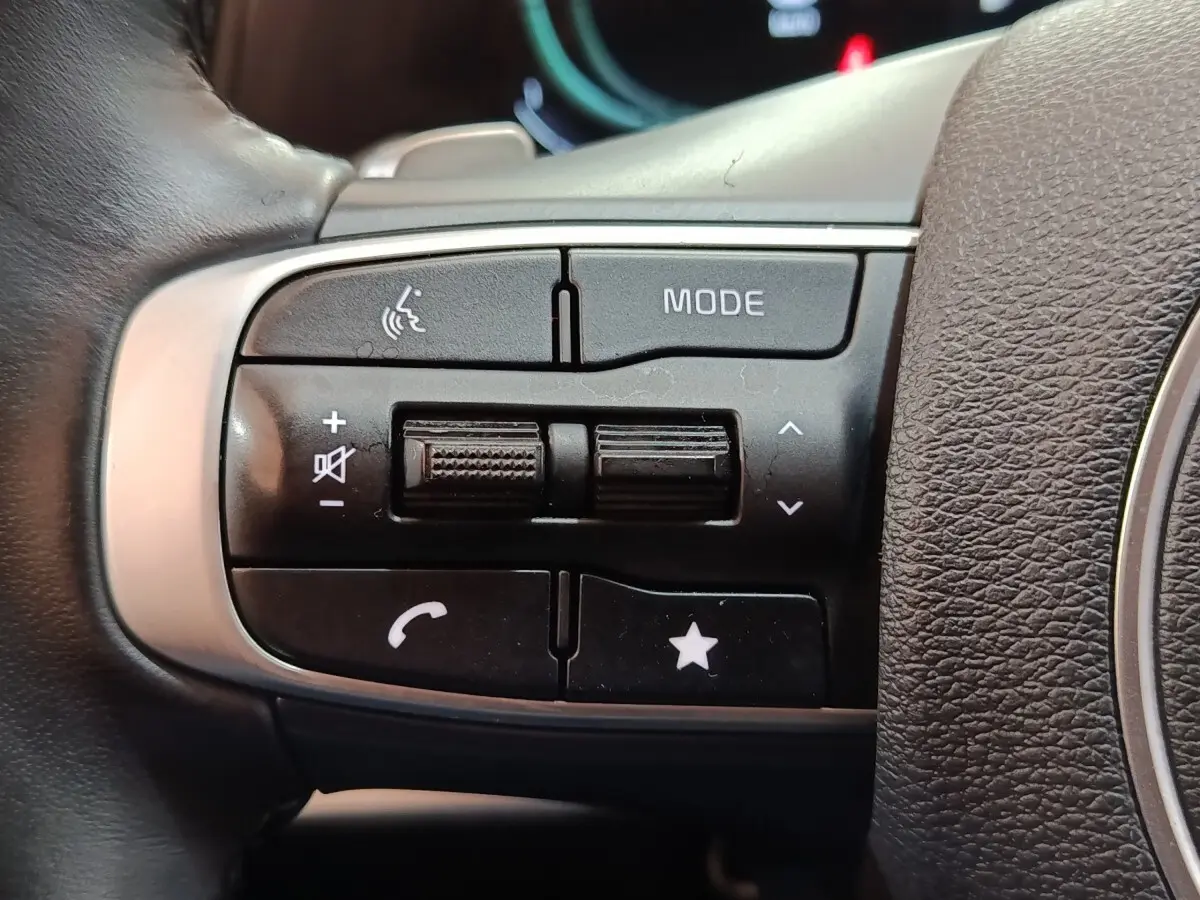 Gros plan sur les commandes multifonctions noires du volant cuir du Kia Sportage hybride rechargeable 2022.