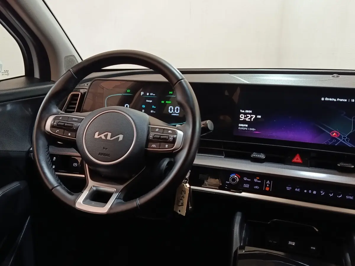 Intérieur du Kia Sportage 2022 vu du poste de conduite, volant cuir multifonctions et grand écran tactile central allumé.