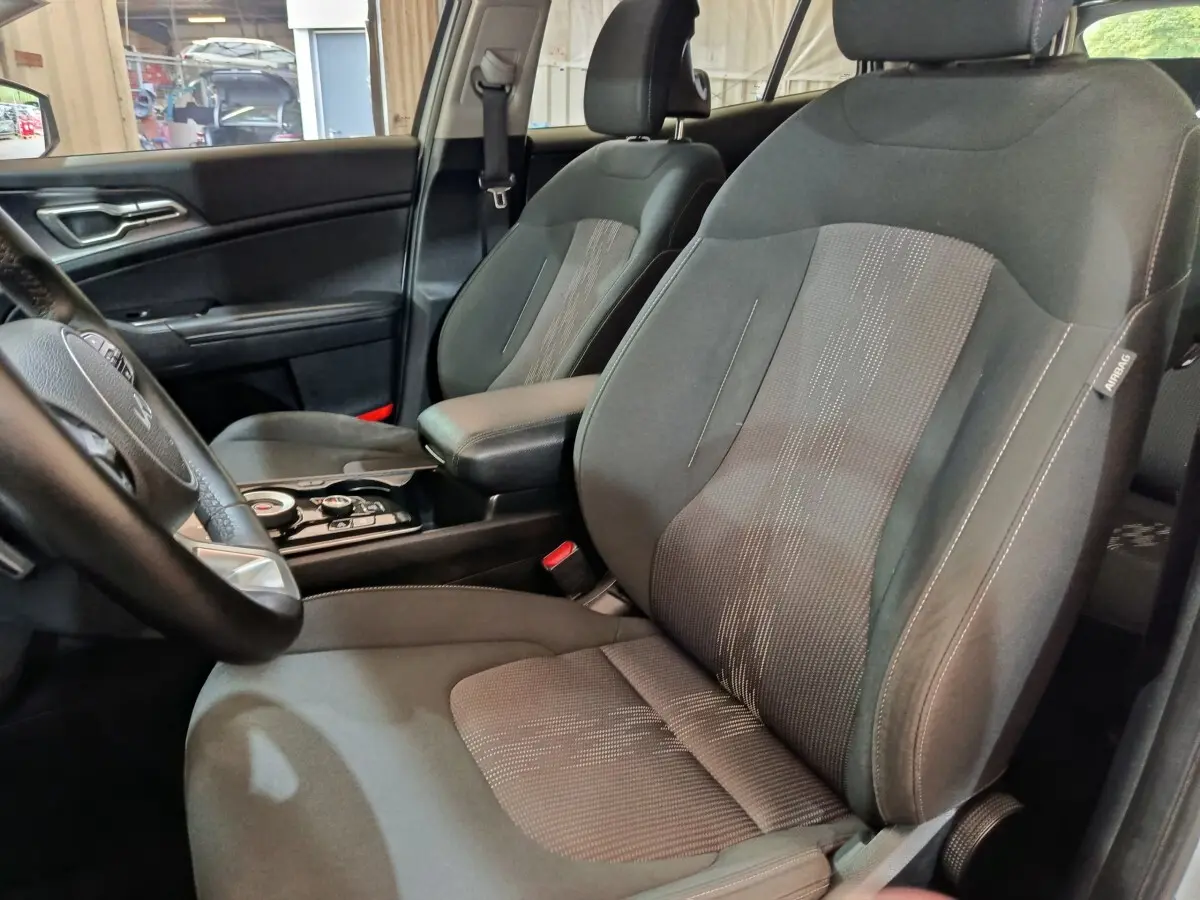 Vue intérieure côté conducteur du Kia Sportage 2022, sièges tissu gris avec accoudoir central noir.
