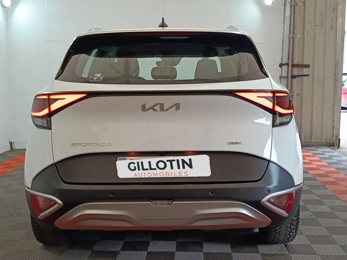 Vue arrière d’un Kia Sportage blanc hybride rechargeable avec feux LED allumés dans un garage.