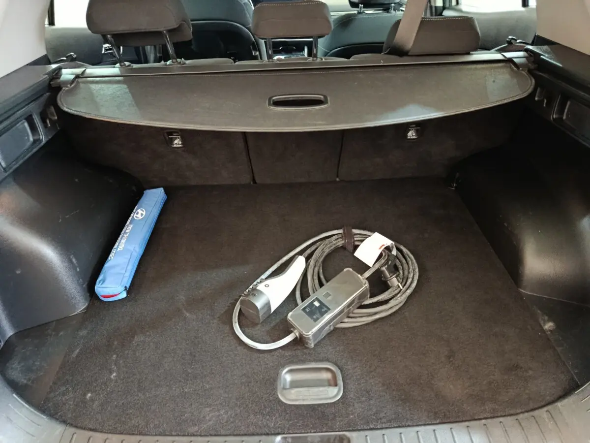 Coffre ouvert d’un KIA Sportage blanc 2022, vue intérieure montrant câble de recharge et rangement noir.