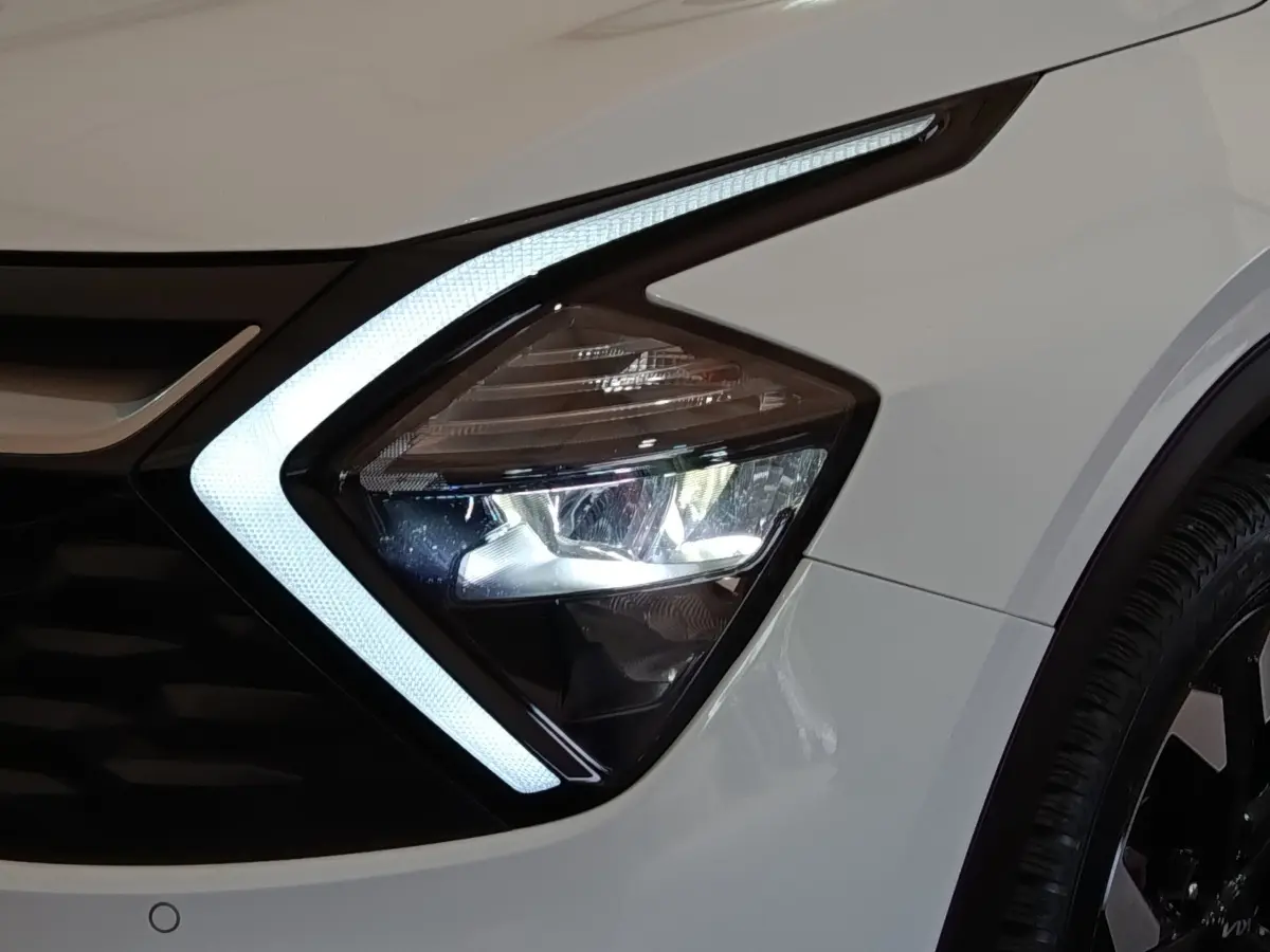 Gros plan sur le phare avant droit blanc du KIA SPORTAGE 2022 avec éclairage LED en forme de flèche.