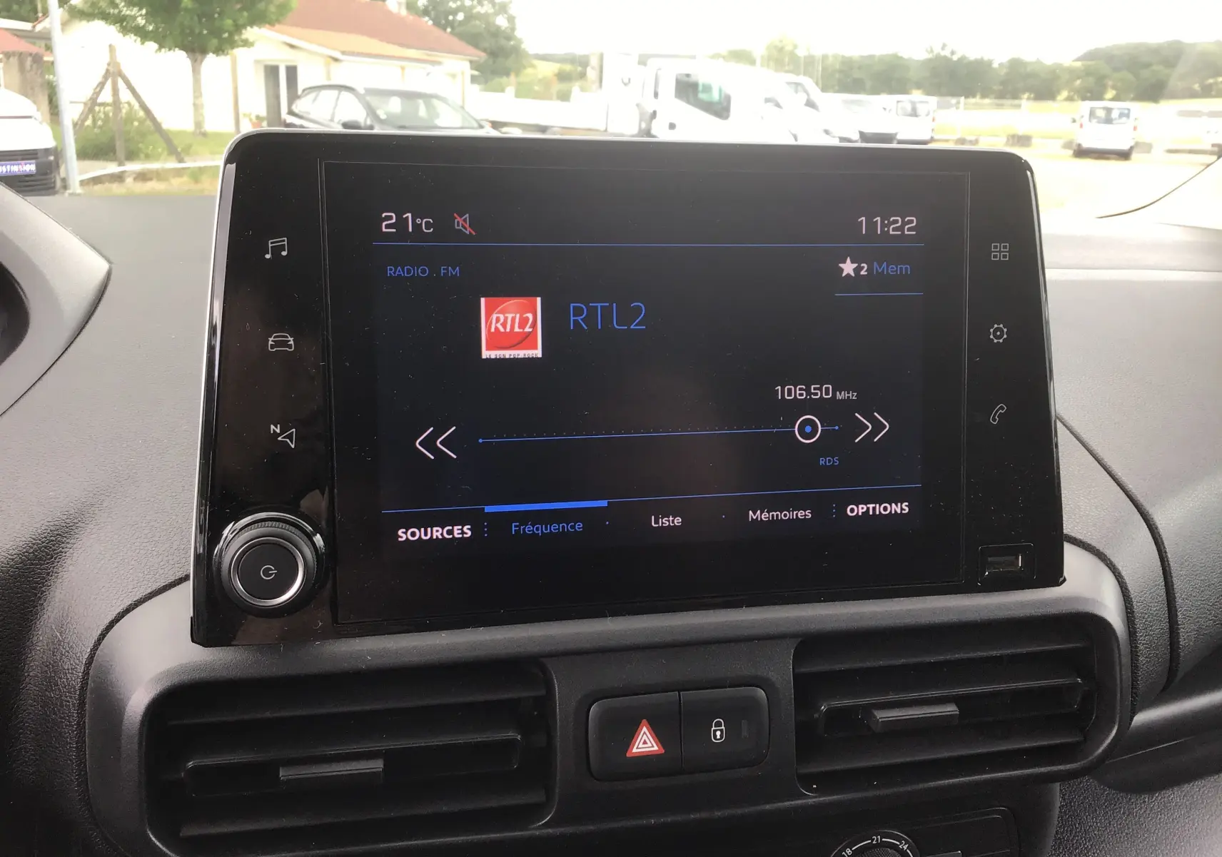 Vue intérieure centrée sur l'écran tactile multimédia du Peugeot Partner blanc, affichant la radio RTL2 à 106,5 MHz.
