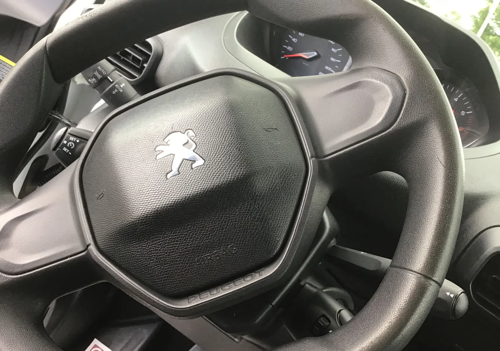 Gros plan sur le volant noir du Peugeot Partner 2022, avec logo lion argenté et tableau de bord en arrière-plan.
