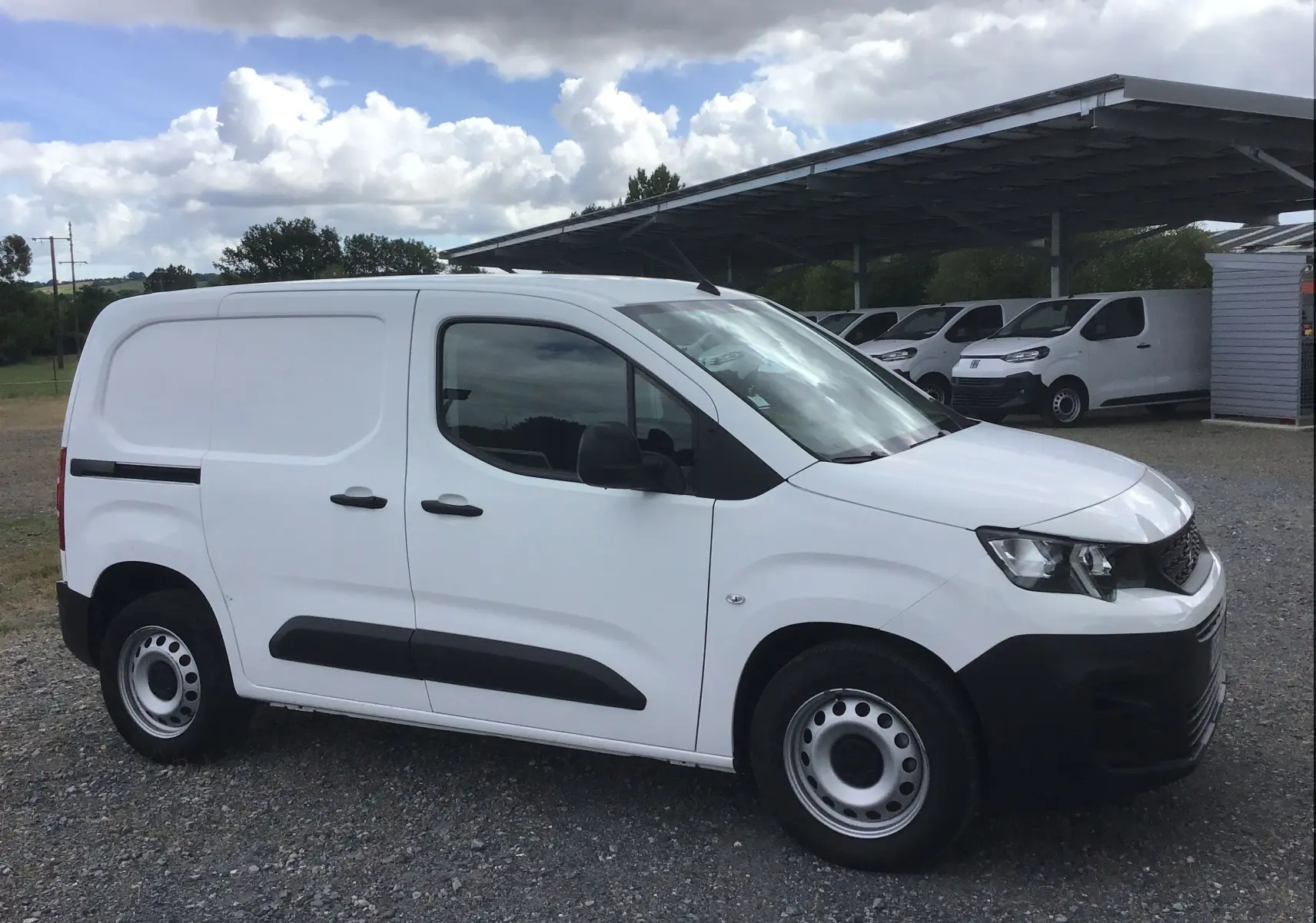 Peugeot Partner blanc vu de profil côté gauche, fourgonnette utilitaire avec protections noires sur portes et pare-chocs.