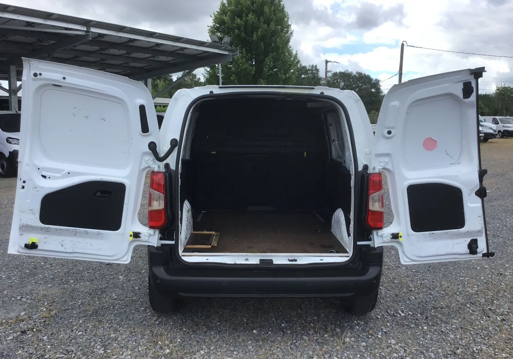 Vue arrière du Peugeot Partner blanc 2022 avec portes battantes ouvertes dévoilant l’espace de chargement vide.