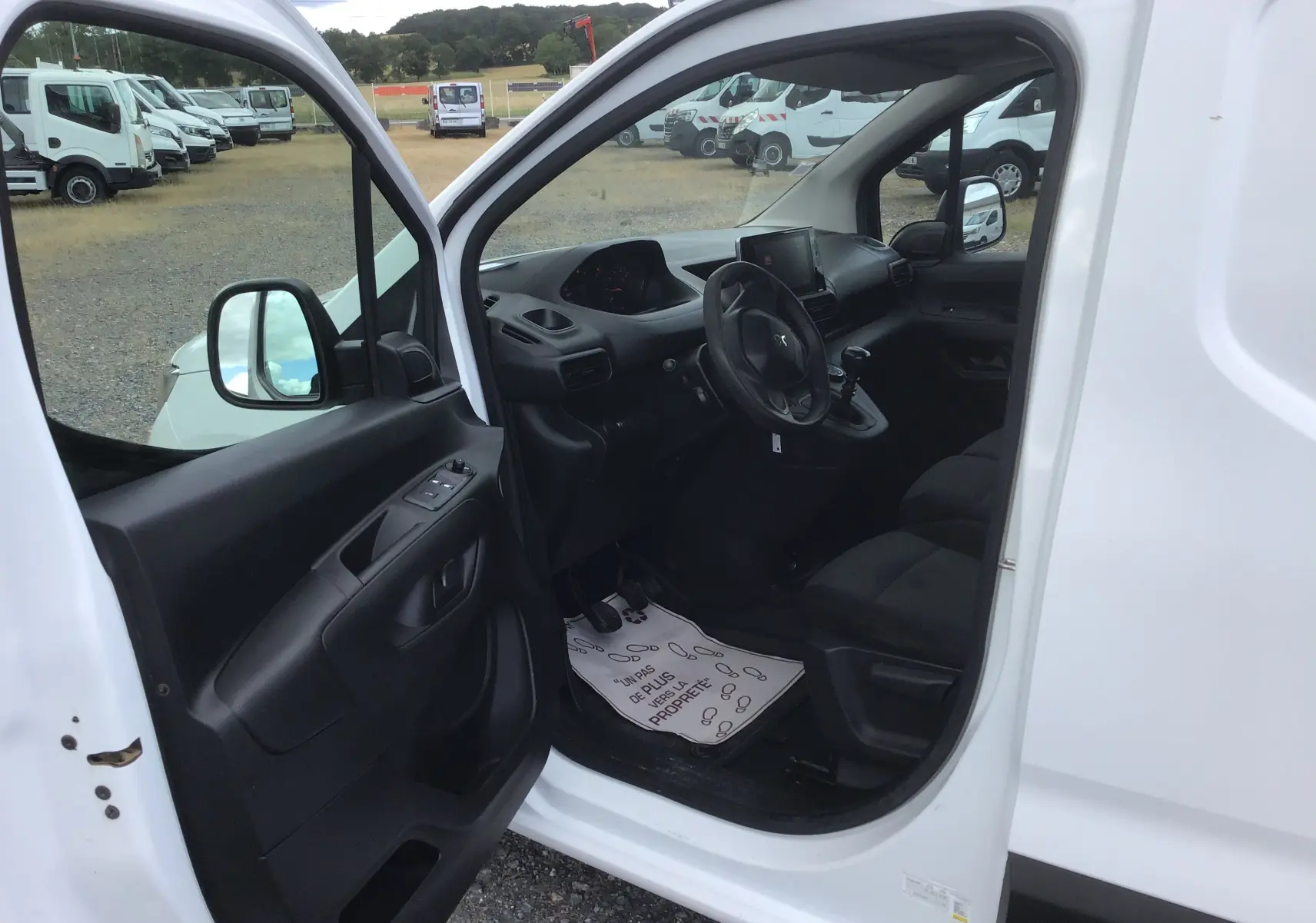 Vue intérieure côté conducteur du Peugeot Partner blanc 2022, montrant tableau de bord et sièges noirs.
