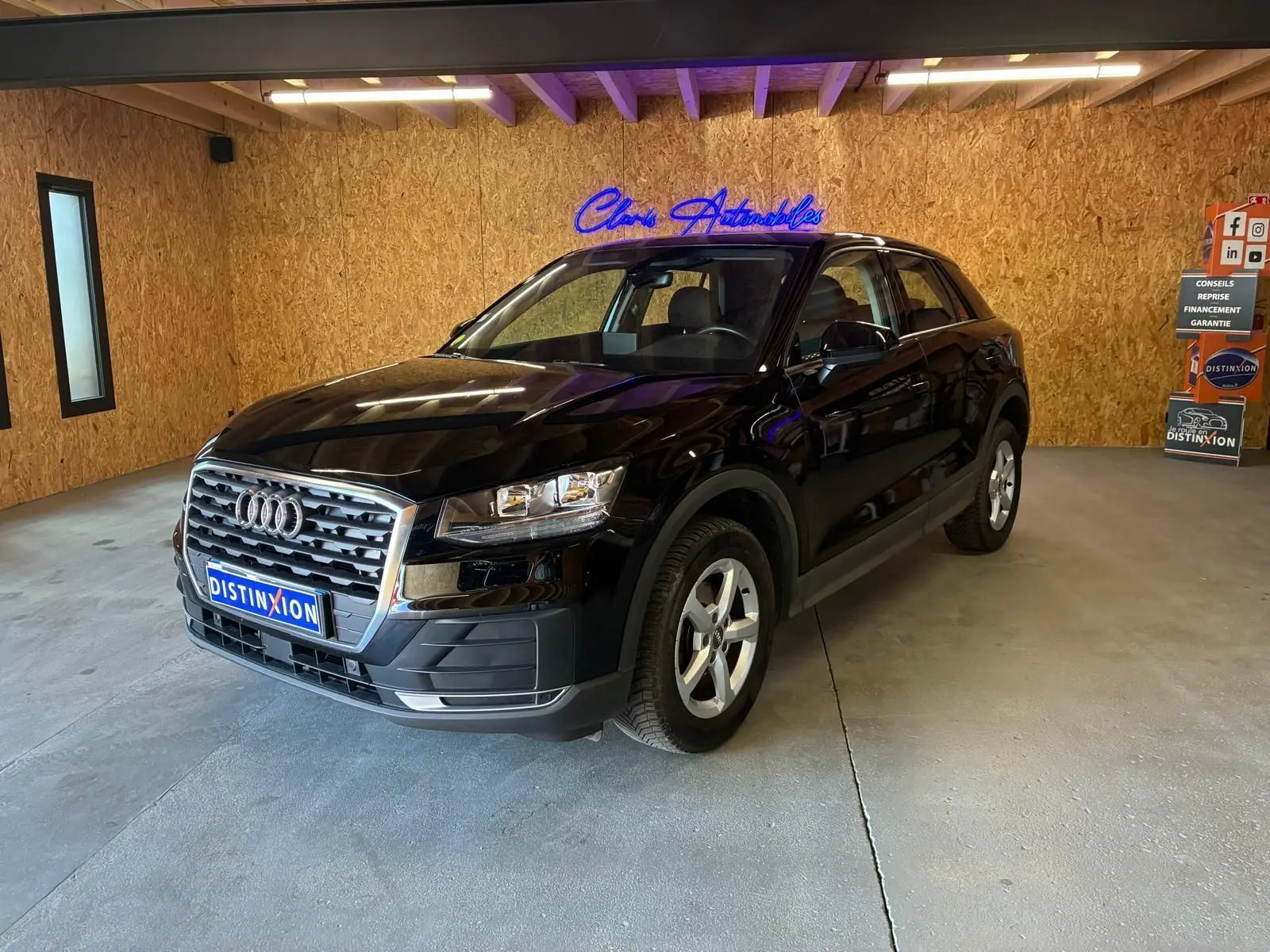 Audi Q2 noir vue 3/4 avant droit dans un showroom avec calandre chromée et jantes argentées.