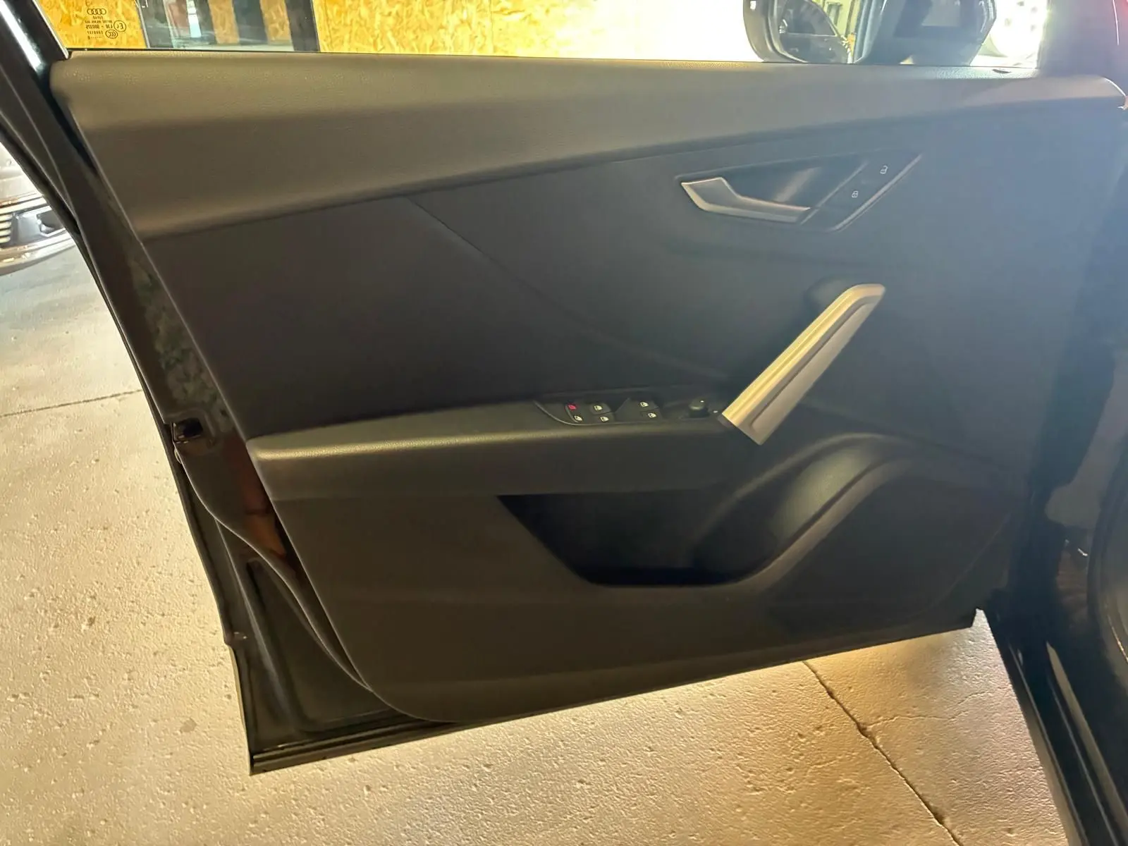 Vue intérieure du panneau de porte avant gauche noir de l'Audi Q2 2020, avec commandes électriques et poignée argentée.