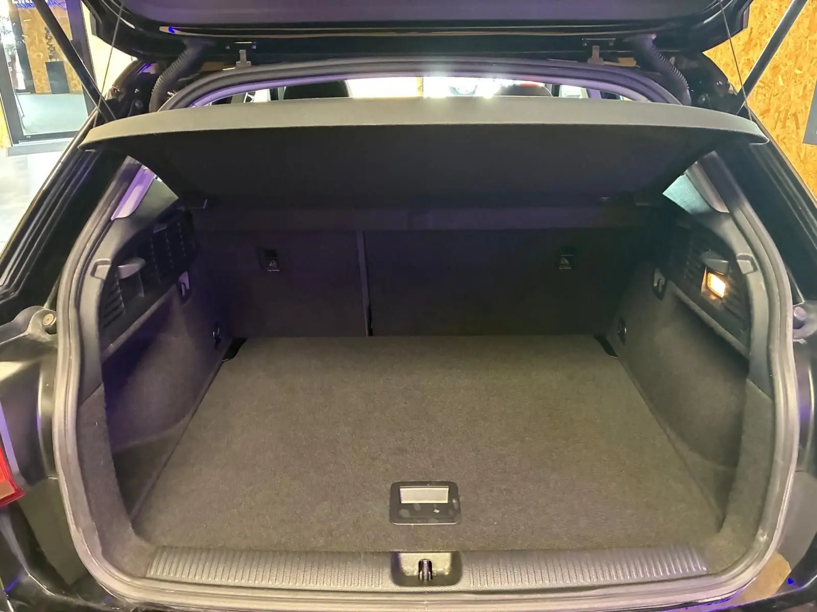 Coffre ouvert vu de l'arrière d'un Audi Q2 noir, montrant un espace de chargement propre et vide avec cache-bagages en place.