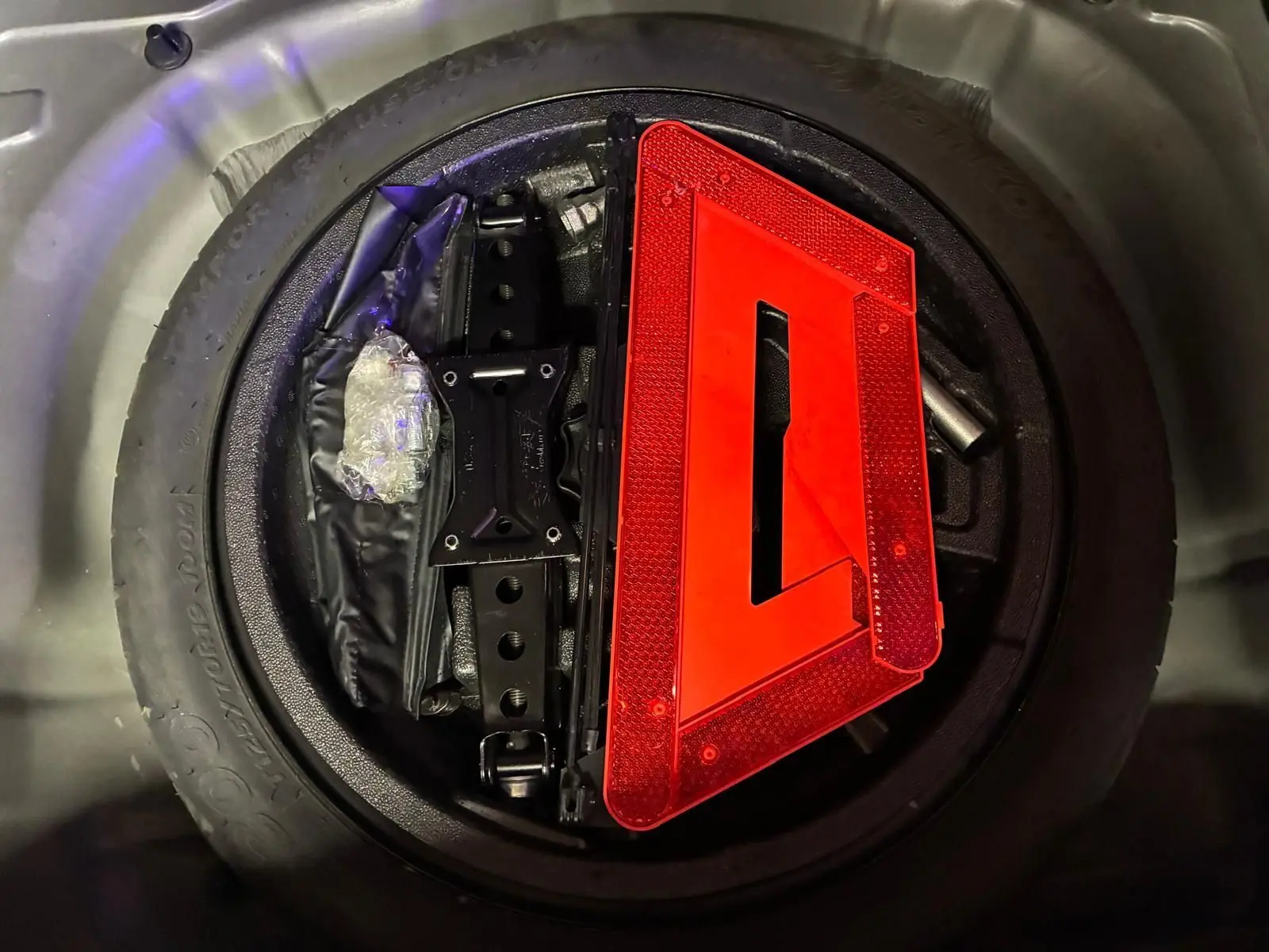 Gros plan sur la roue de secours noire d’un Audi Q2 2020 avec triangle de signalisation rouge posé dessus.