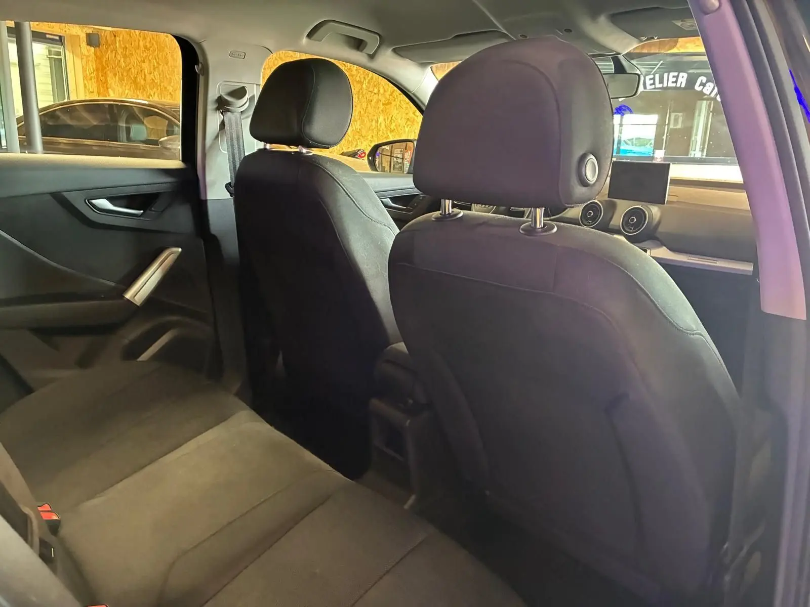Vue intérieure arrière de l’Audi Q2 noire, montrant les sièges en tissu noir et le tableau de bord avec écran central.