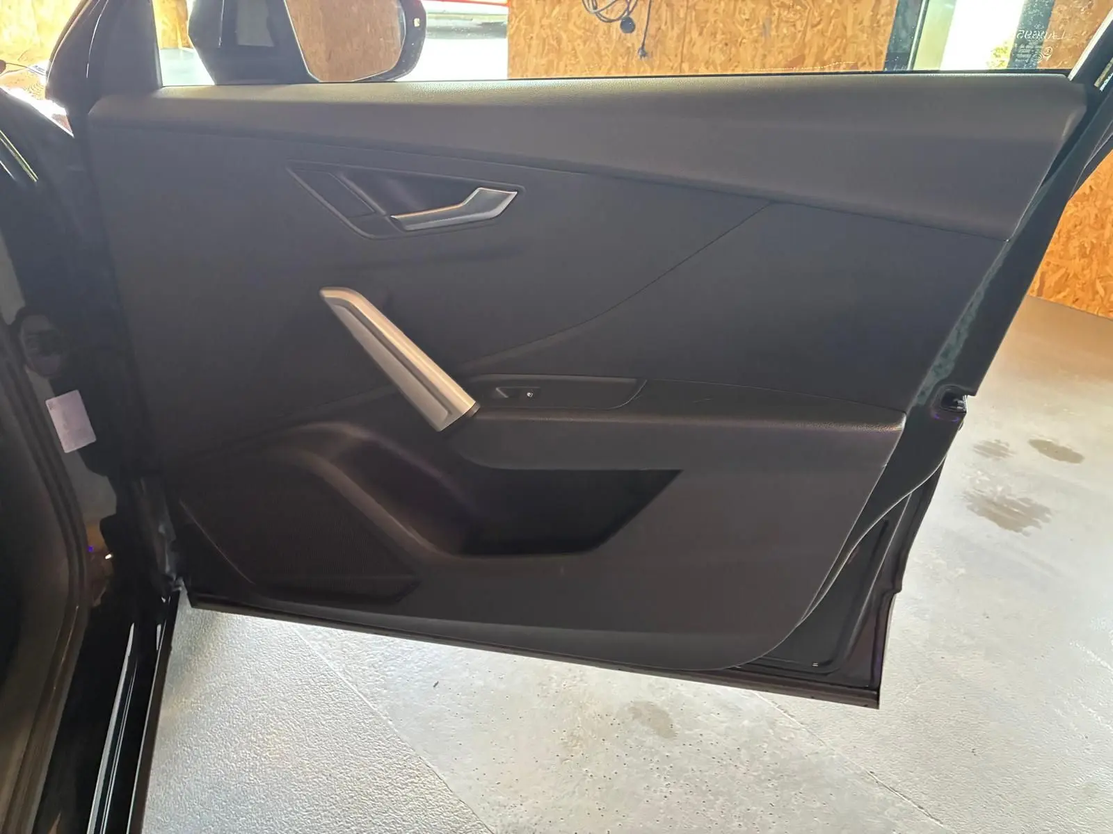 Vue intérieure de la porte côté gauche noire de l'Audi Q2 30 1.6 TDI 2020 avec poignée argentée et habillage tissu.