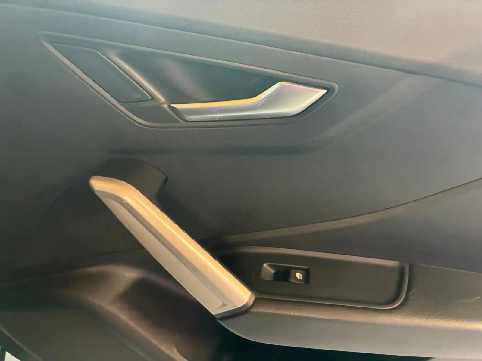 Gros plan sur la poignée intérieure côté gauche de la porte noire d’un Audi Q2 2020, avec bouton de commande de vitre.