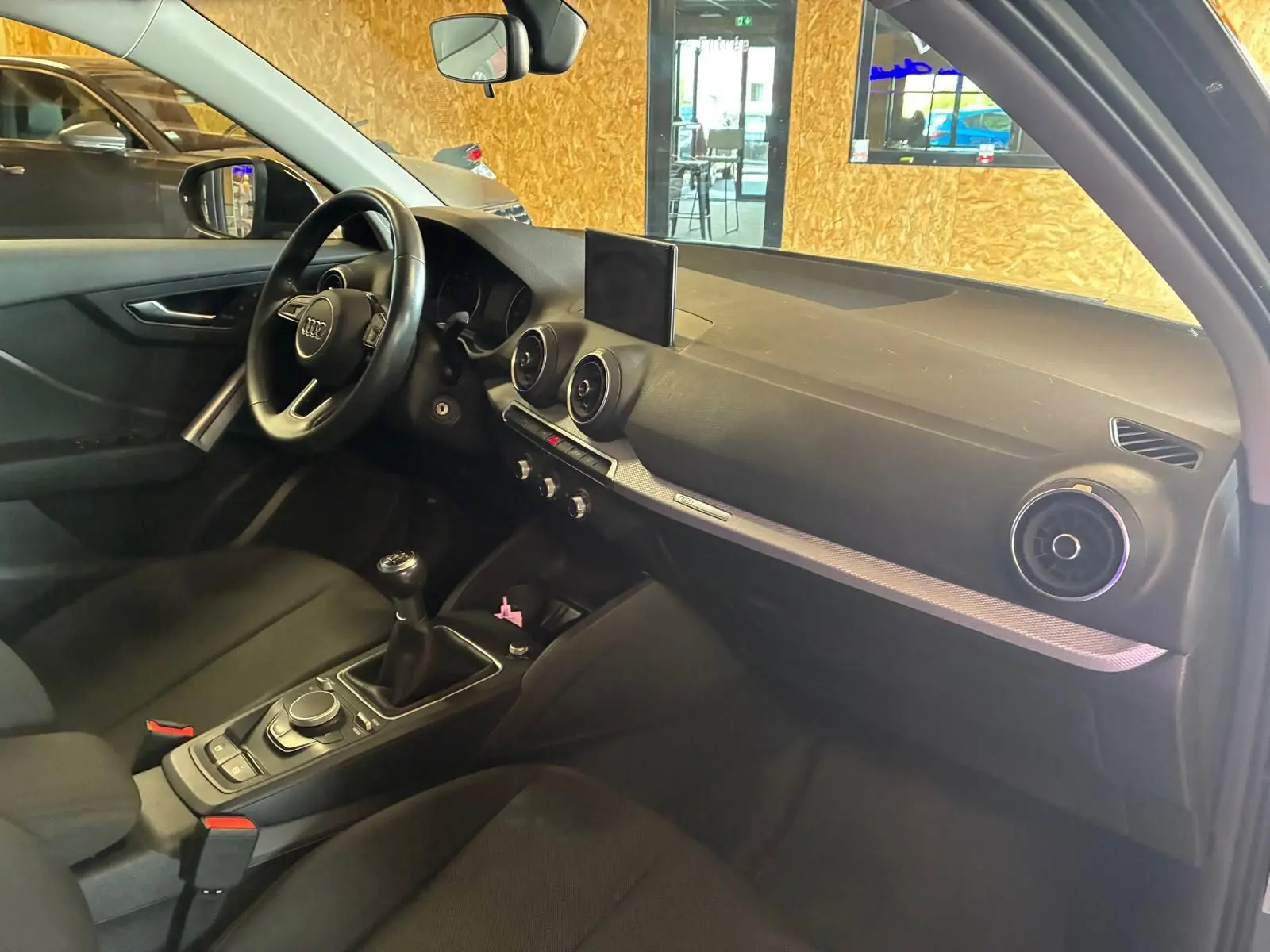 Intérieur noir de l’Audi Q2 30 1.6 TDI 2020 vu côté conducteur, avec tableau de bord et levier de vitesses manuel.