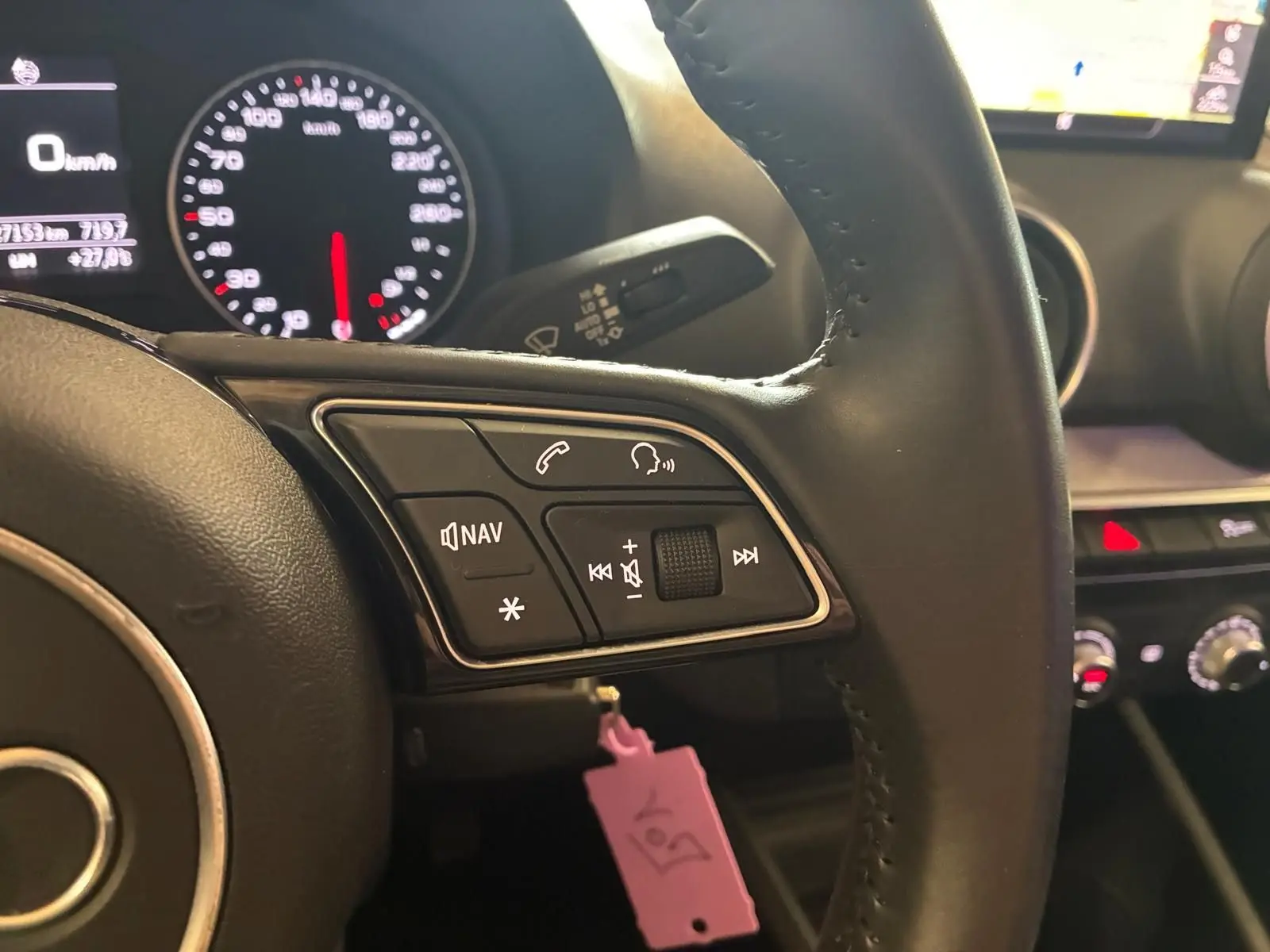 Gros plan sur le volant noir de l'Audi Q2 2020, avec commandes audio et tableau de bord lumineux en arrière-plan.