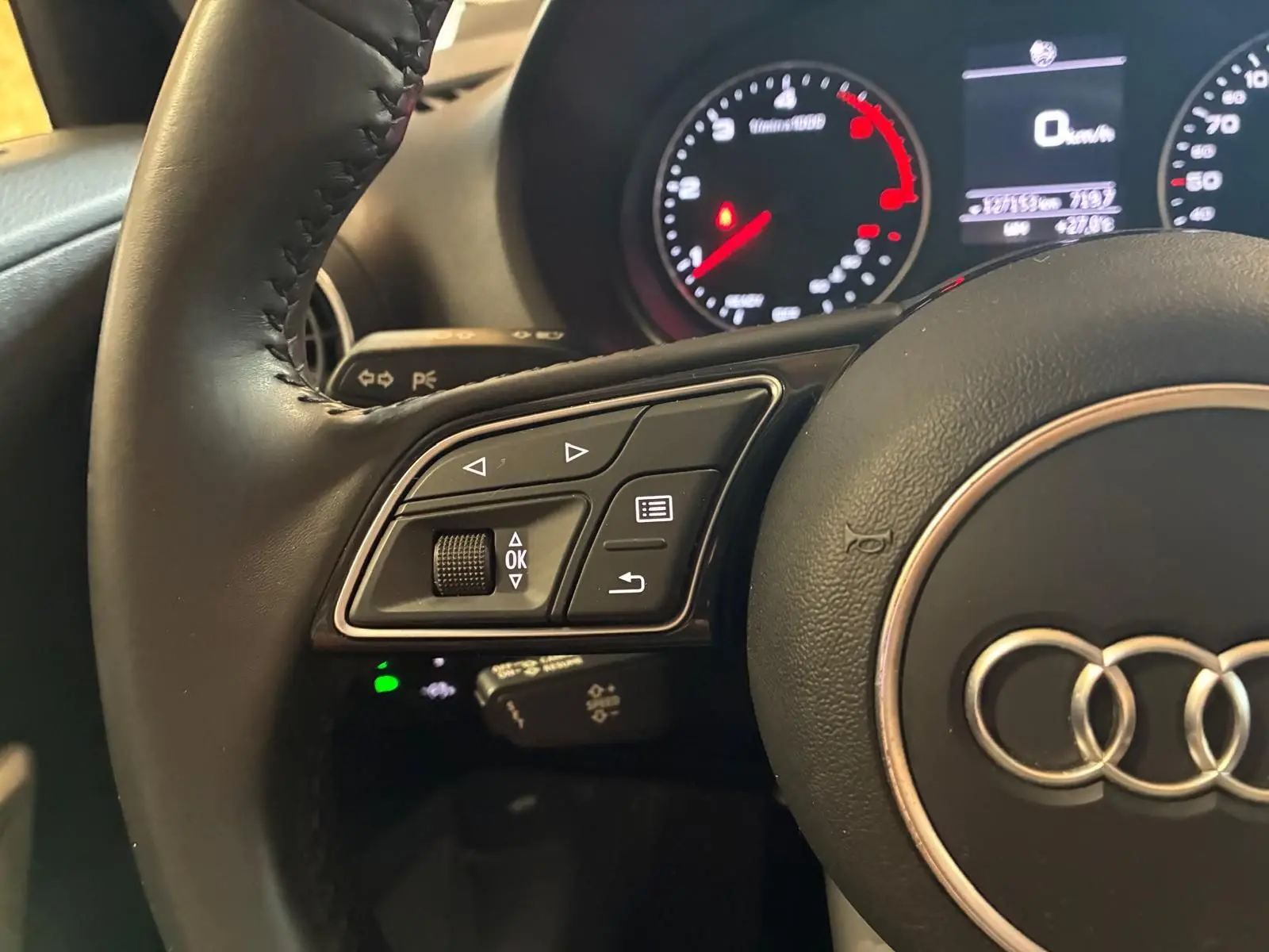 Gros plan sur le volant noir d’un Audi Q2 2020, montrant les commandes à gauche et le tableau de bord lumineux en arrière-plan.