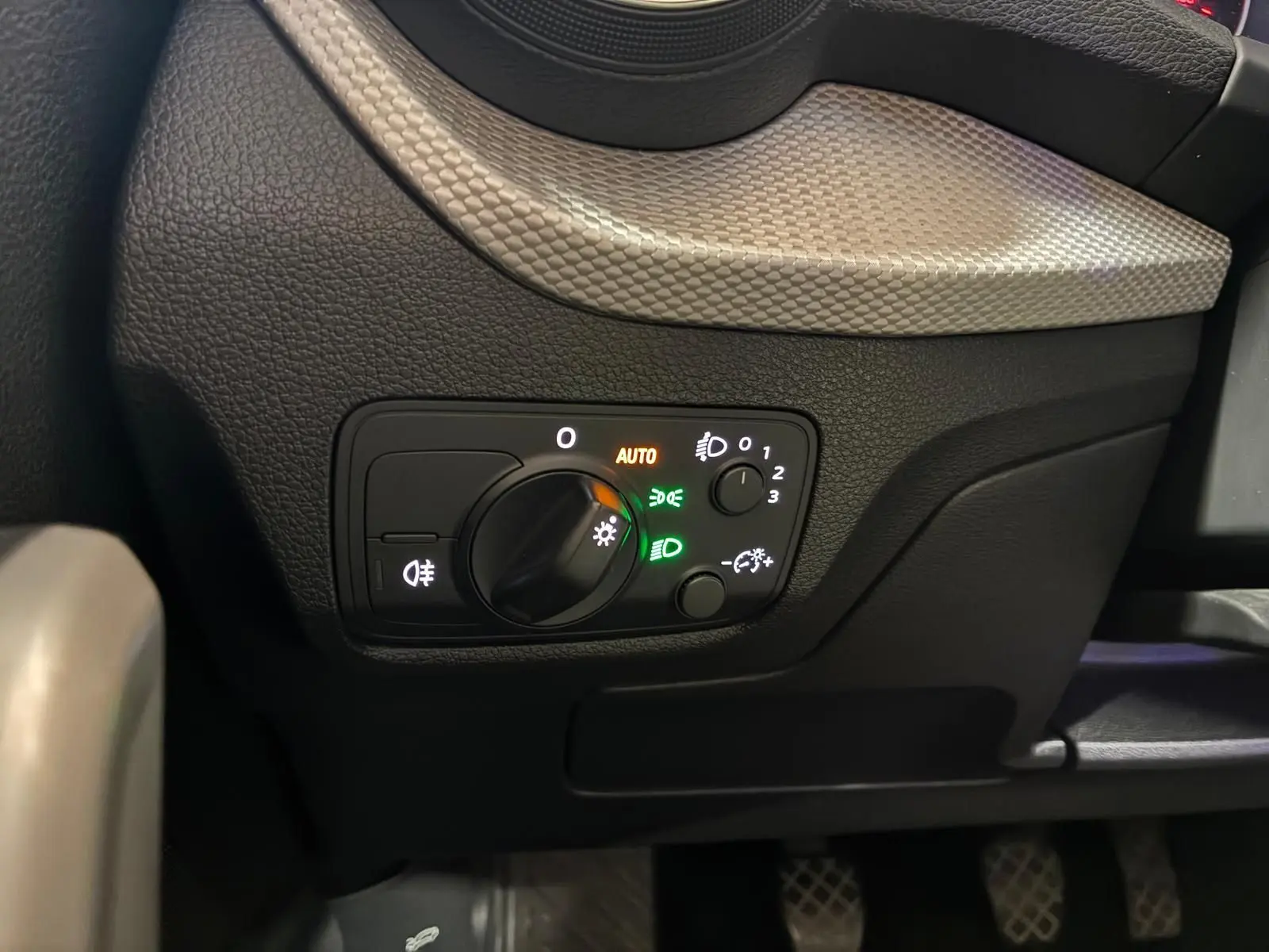 Gros plan sur le panneau de commande des phares de l’Audi Q2 30 1.6 TDI 116 BVM6 Design, intérieur noir.