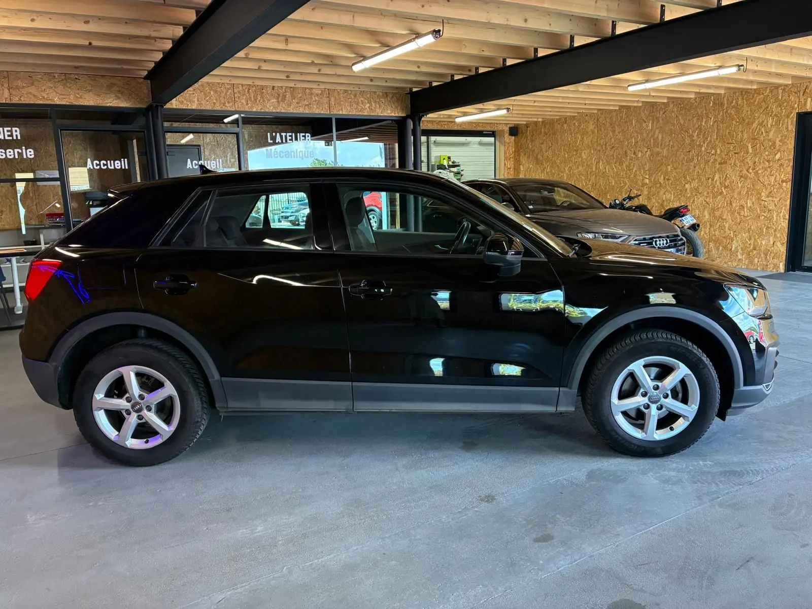 Audi Q2 noire vue de profil côté gauche dans un garage, soulignant ses jantes alliage et sa silhouette compacte.