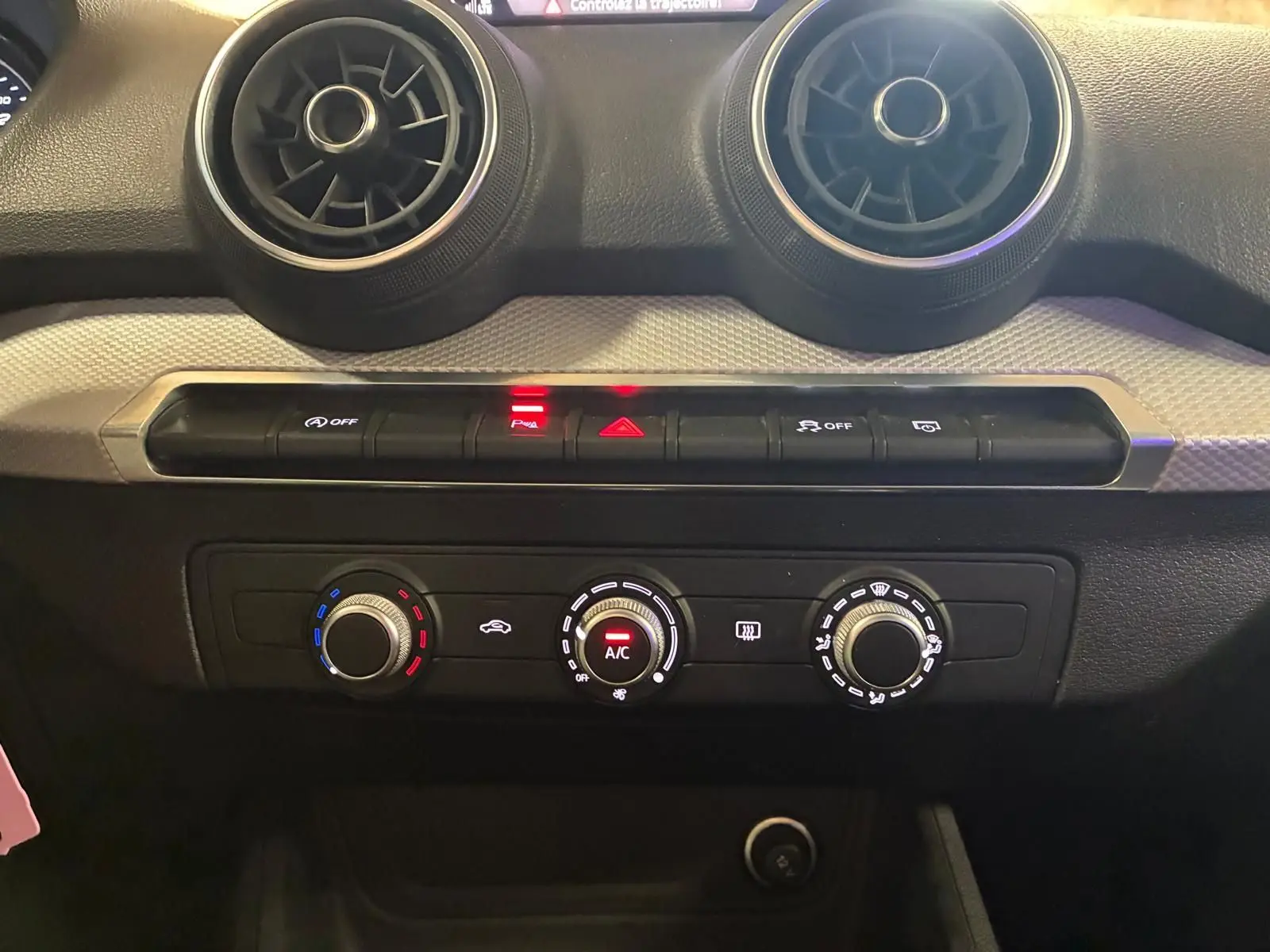 Vue rapprochée du tableau de bord noir de l'Audi Q2 2020, mettant en valeur les commandes de climatisation et les aérateurs ronds.