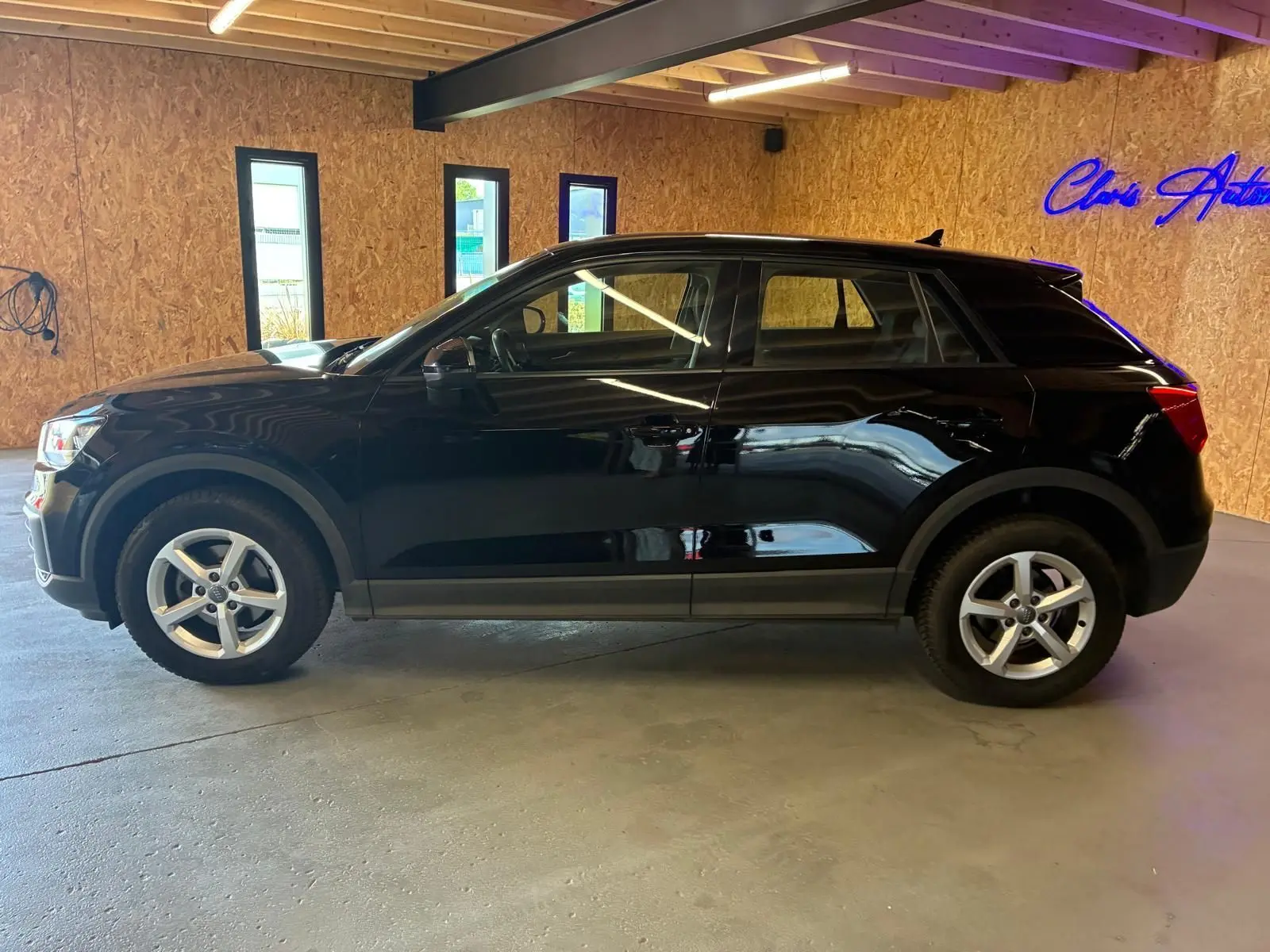Audi Q2 noir vue de profil côté gauche dans un garage avec murs en bois et éclairage intérieur.