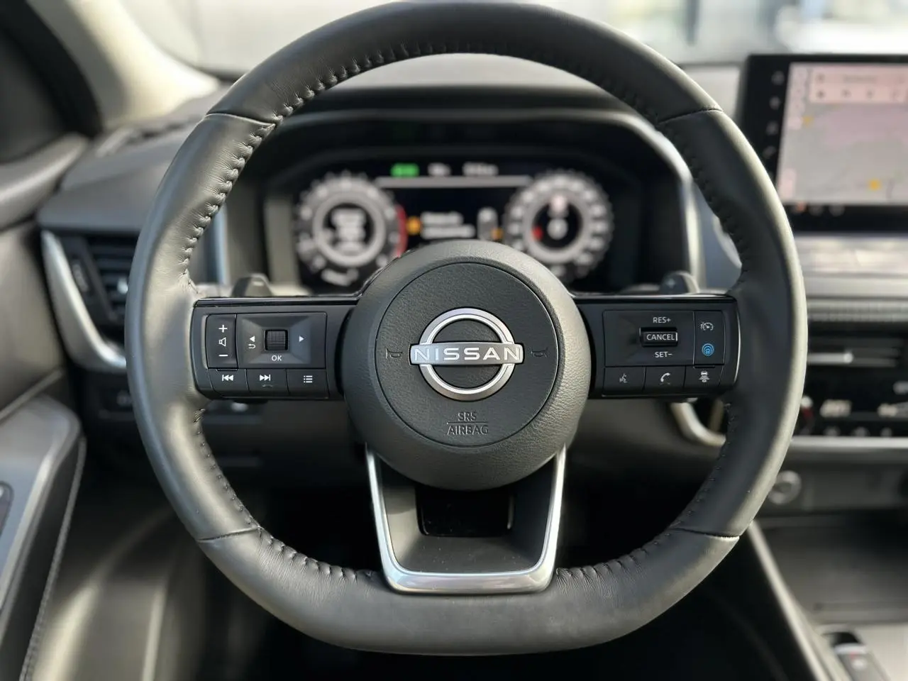 Vue rapprochée du volant cuir noir du Nissan Qashqai 2025 avec commandes intégrées et tableau de bord numérique flou.