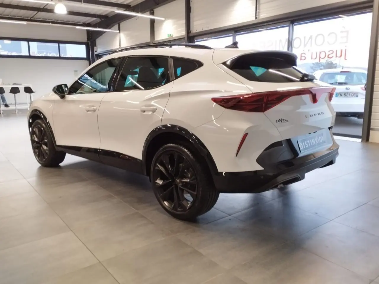 Vue 3/4 arrière droite d’un CUPRA Formentor blanc Nevada avec jantes noires et bandeau lumineux arrière Tri-LED.