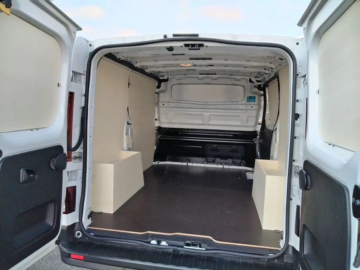 Vue arrière du Nissan Primastar blanc 2025 avec portes ouvertes montrant l'aménagement bois intérieur du coffre.