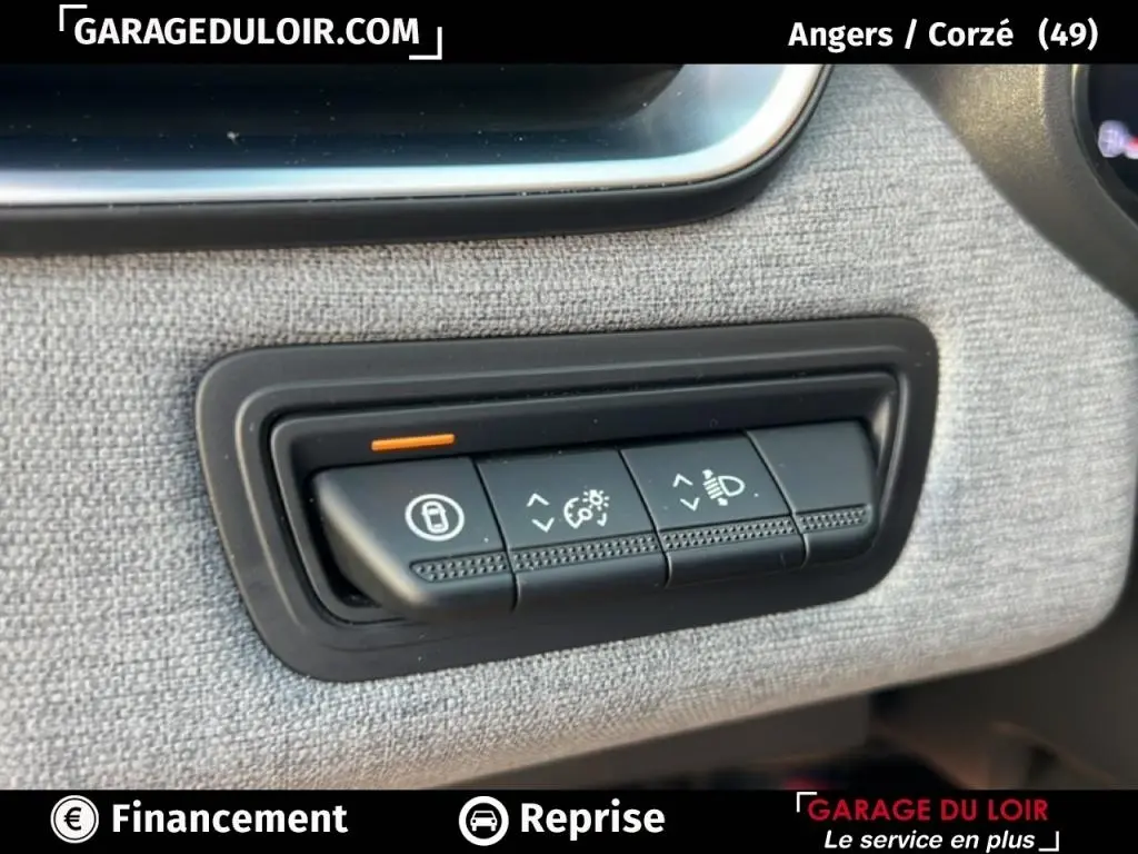 Gros plan sur les commandes de réglage des feux et verrouillage, tableau de bord tissu gris d’une Renault Clio noire.