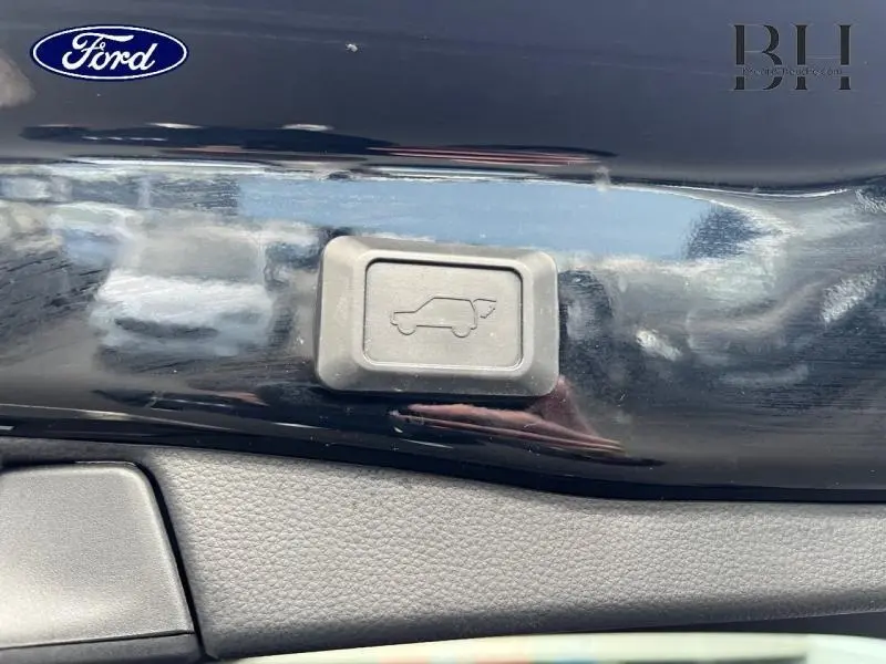 Bouton d'ouverture électrique du coffre sur une surface noire métallisée brillante d'un Toyota RAV4.