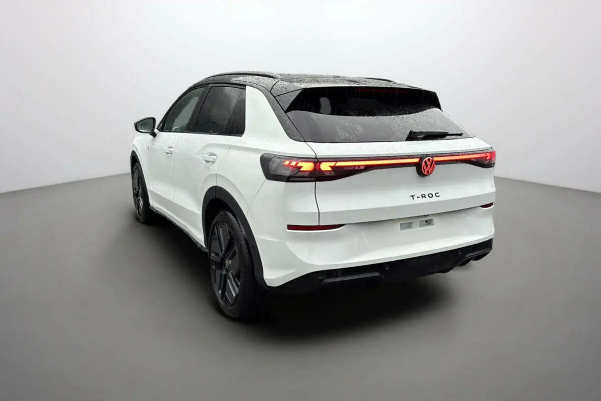 Volkswagen T-Roc blanc toit noir en 3/4 arrière droit avec feux arrière allumés et jantes noires.