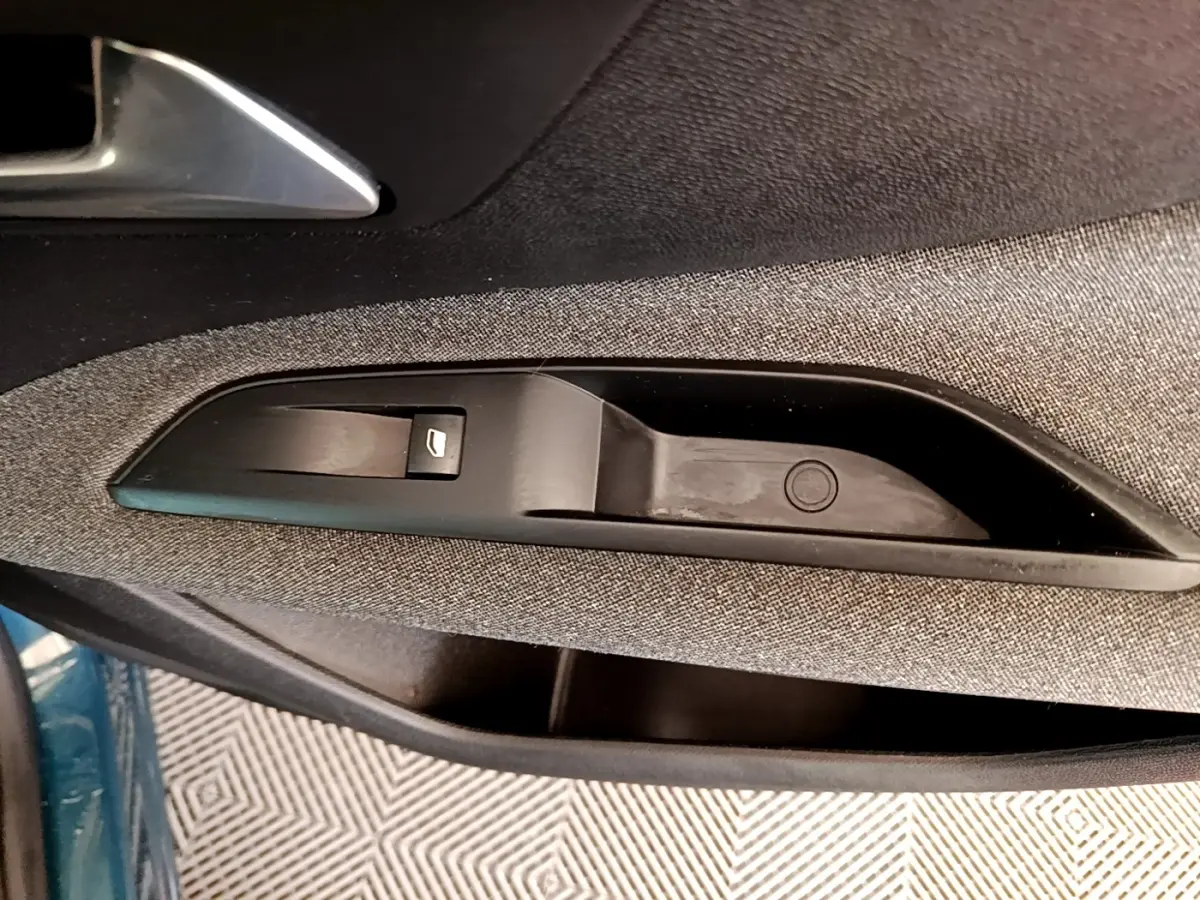 Gros plan sur la commande de lève-vitre côté gauche d’une Peugeot 3008 bleu, tissu gris et plastique noir.
