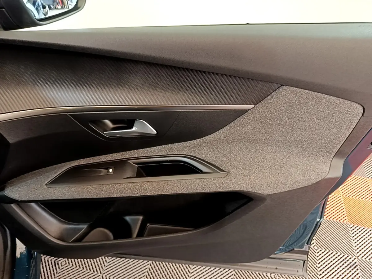 Vue intérieure de la porte avant gauche du Peugeot 3008 bleu, avec habillage tissu et insert imitation carbone.