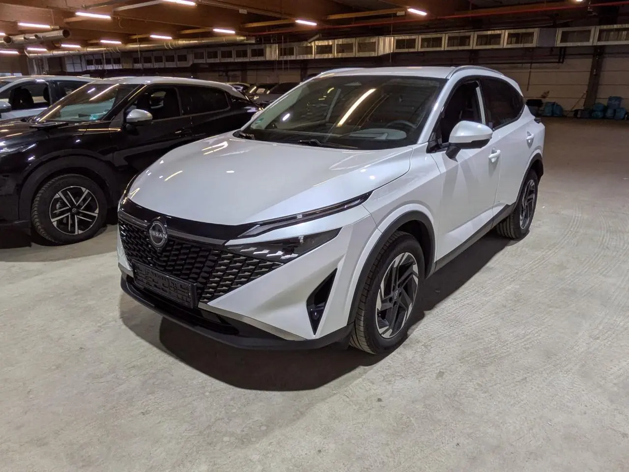Nissan Qashqai blanc nacré vu en 3/4 avant droit, avec calandre noire et jantes alliage 18 pouces.