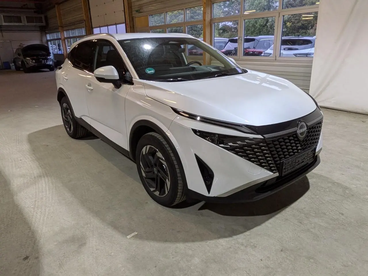 Nissan Qashqai blanc nacré vu en 3/4 avant droit, avec calandre noire et jantes alliage 18 pouces.