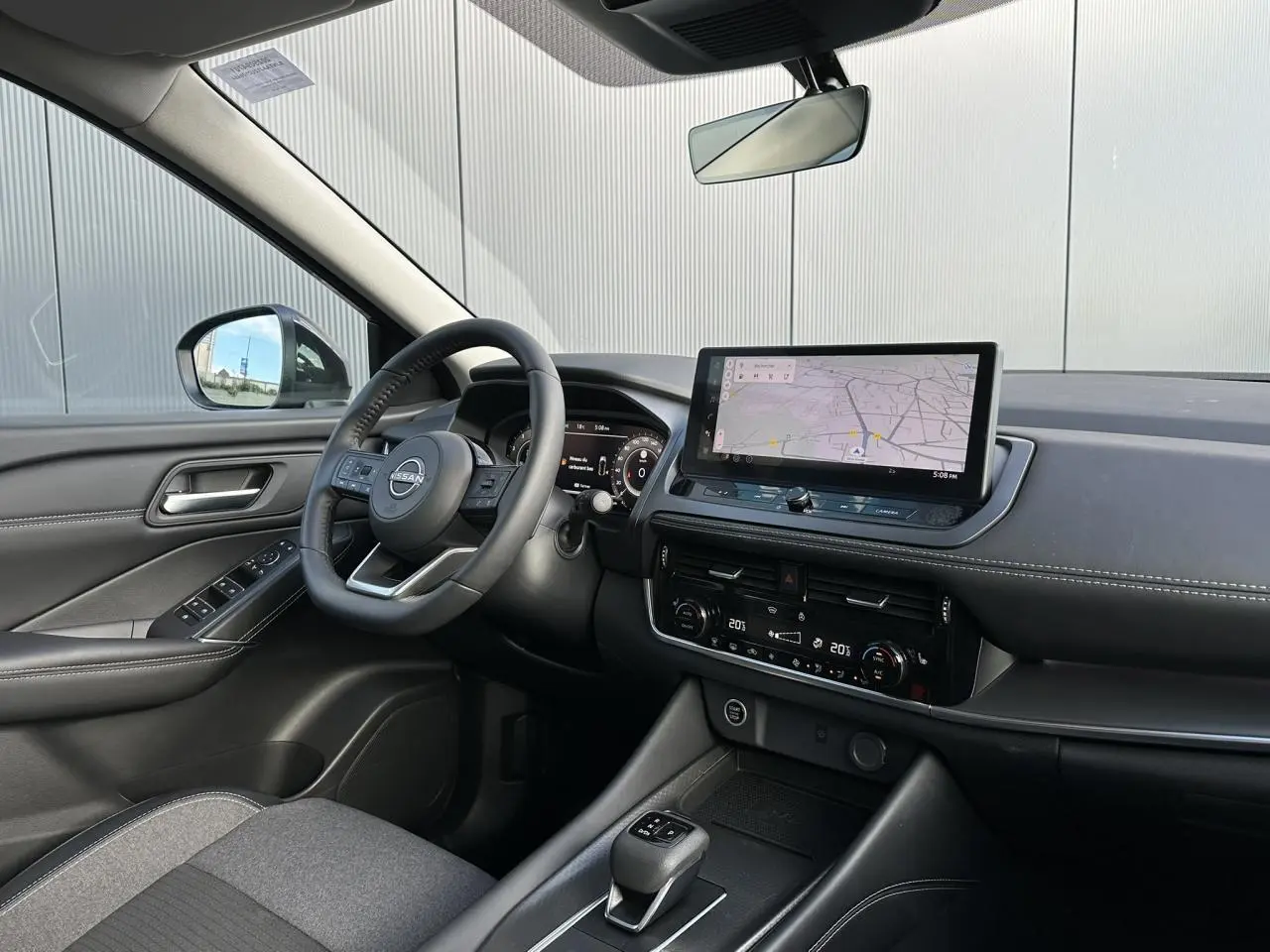 Vue intérieure côté conducteur du Nissan Qashqai blanc nacré 2025, avec tableau de bord numérique et écran tactile de navigation.