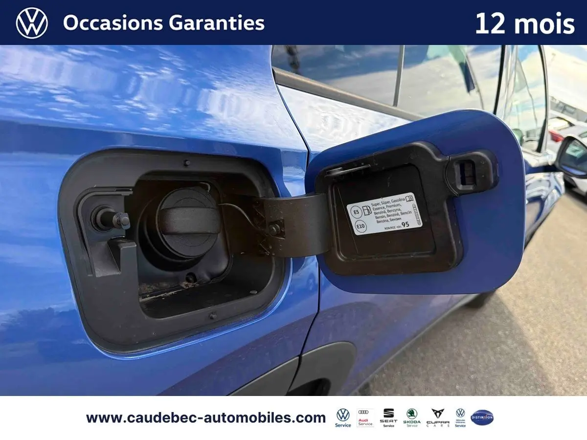 Gros plan sur la trappe à carburant ouverte côté gauche d’un Volkswagen T-Roc bleu métallisé stationné.
