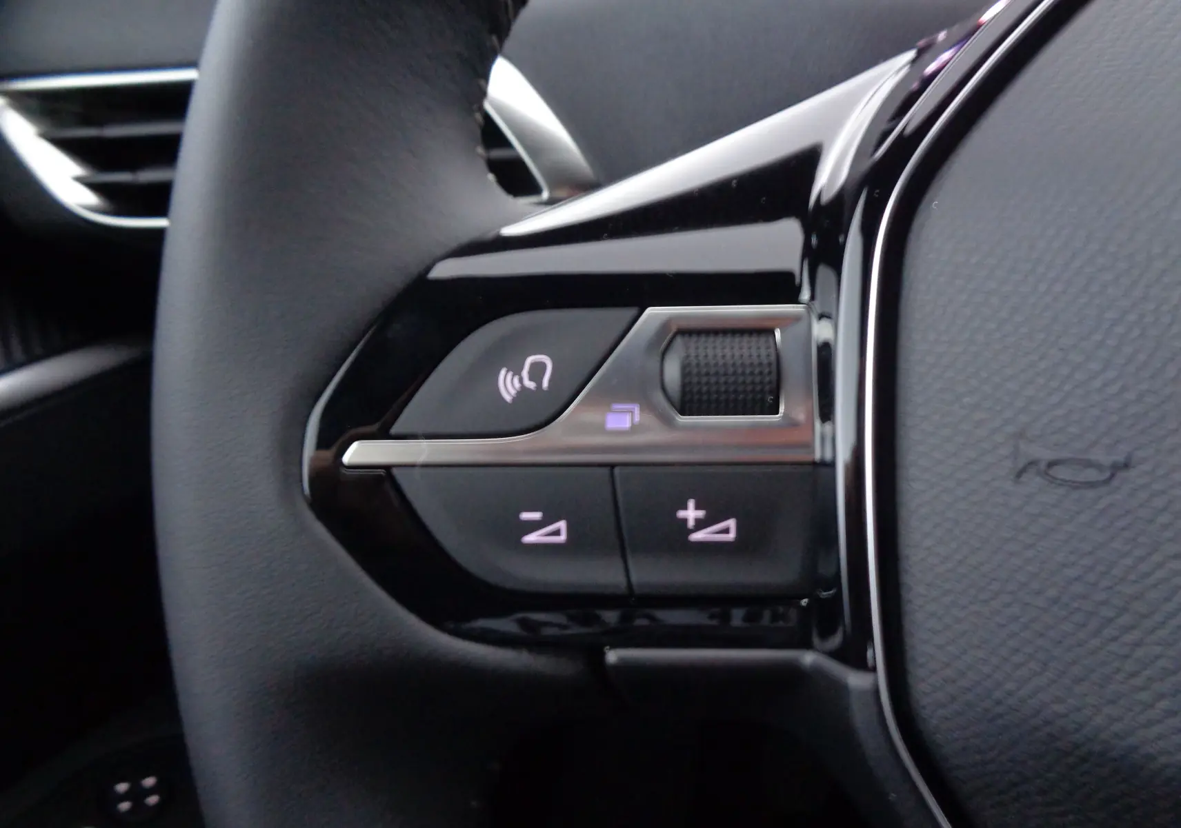 Gros plan sur les commandes gauche du volant cuir noir du Peugeot 3008 gris Artense 2023, boutons de volume et appel.
