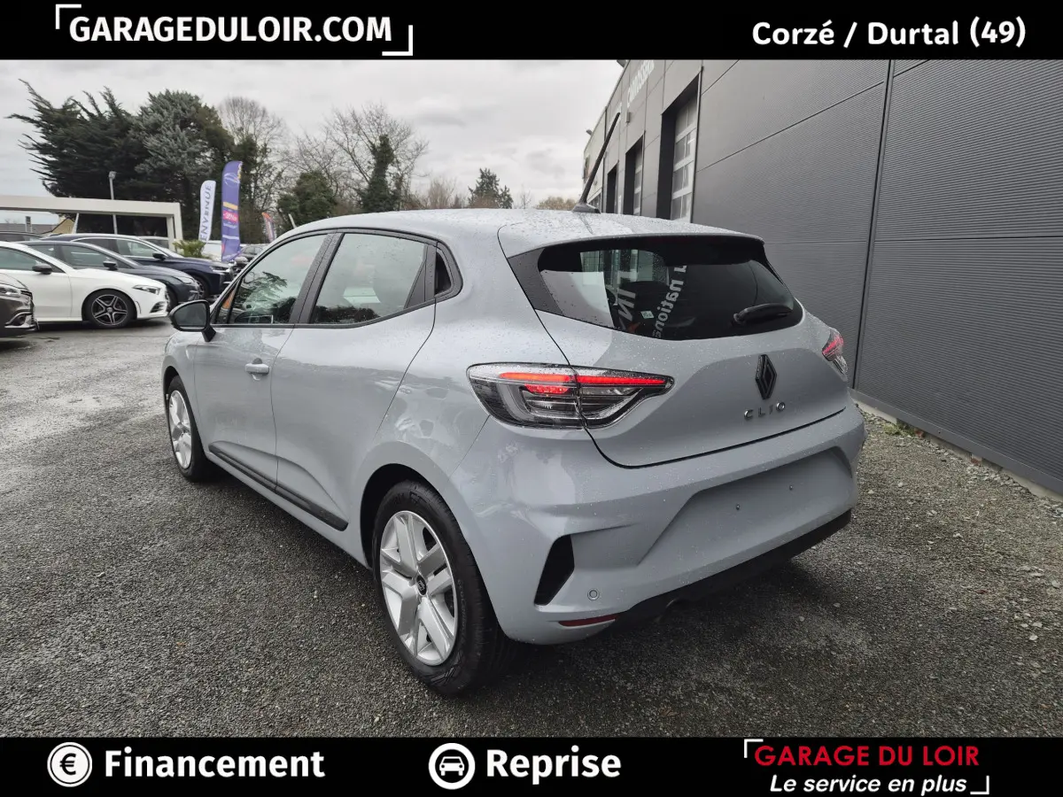 Vue 3/4 arrière droite d'une Renault Clio gris clair 2025 garée devant un bâtiment gris.