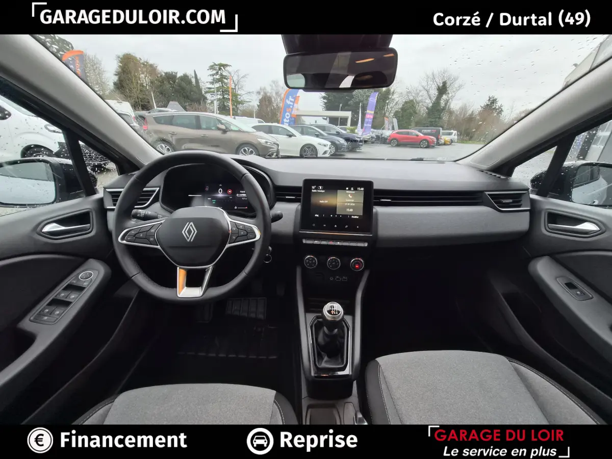 Vue intérieure avant de la Renault Clio gris clair 2025, volant multifonctions cuir et écran tactile central visible.