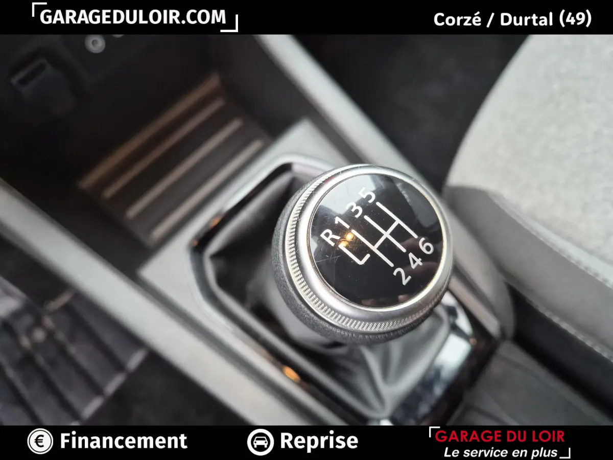 Gros plan sur le levier de vitesse manuel noir de la Renault Clio gris clair, avec marquages blancs visibles.