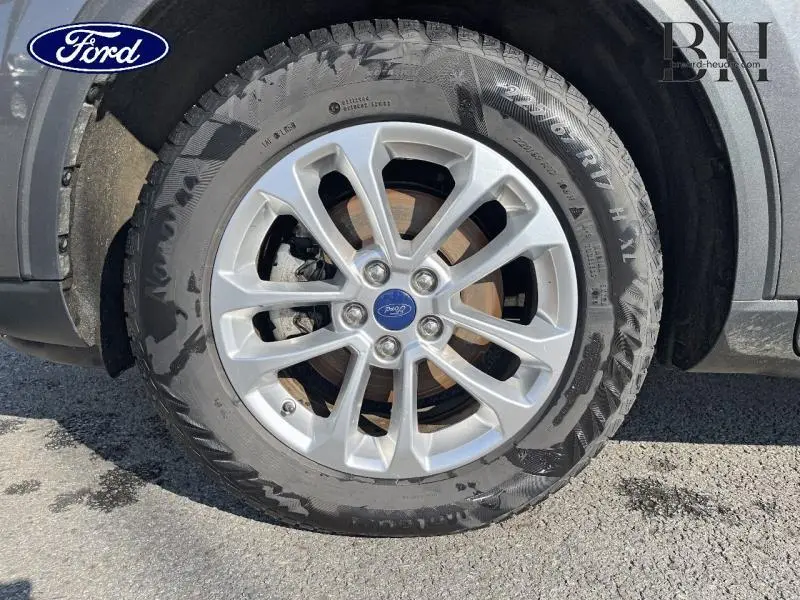 Gros plan sur la roue avant gauche du Ford Kuga gris métallisé avec jante alu et logo Ford au centre.