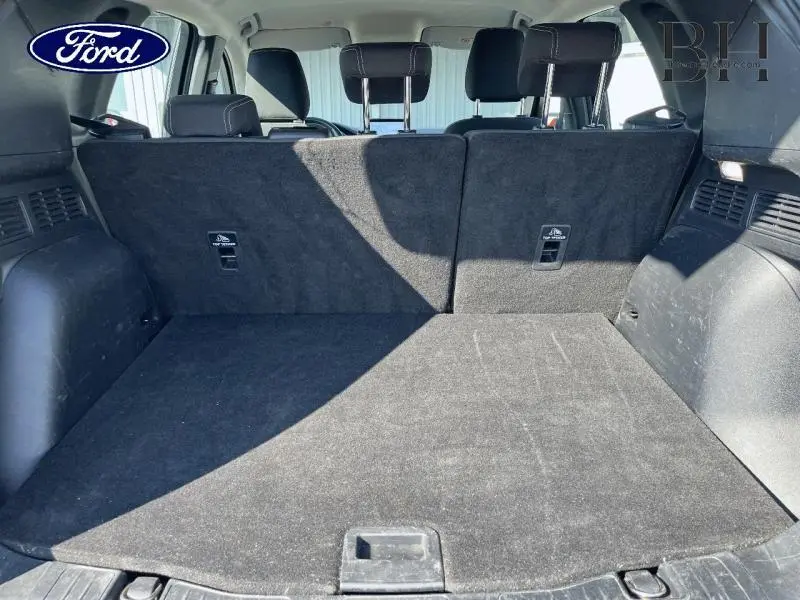 Vue du coffre spacieux et tapis noir du Ford Kuga 2022 gris Magnetic Métallisée, avec banquette arrière relevée.