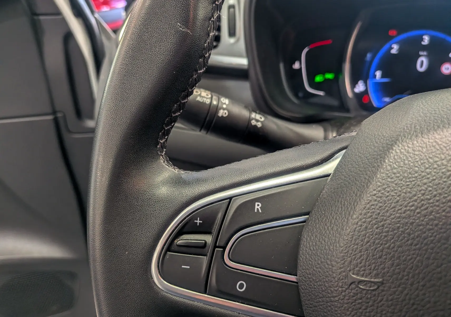 Gros plan sur les commandes gauche du volant noir du Renault Kadjar 2021, tableau de bord numérique en arrière-plan.