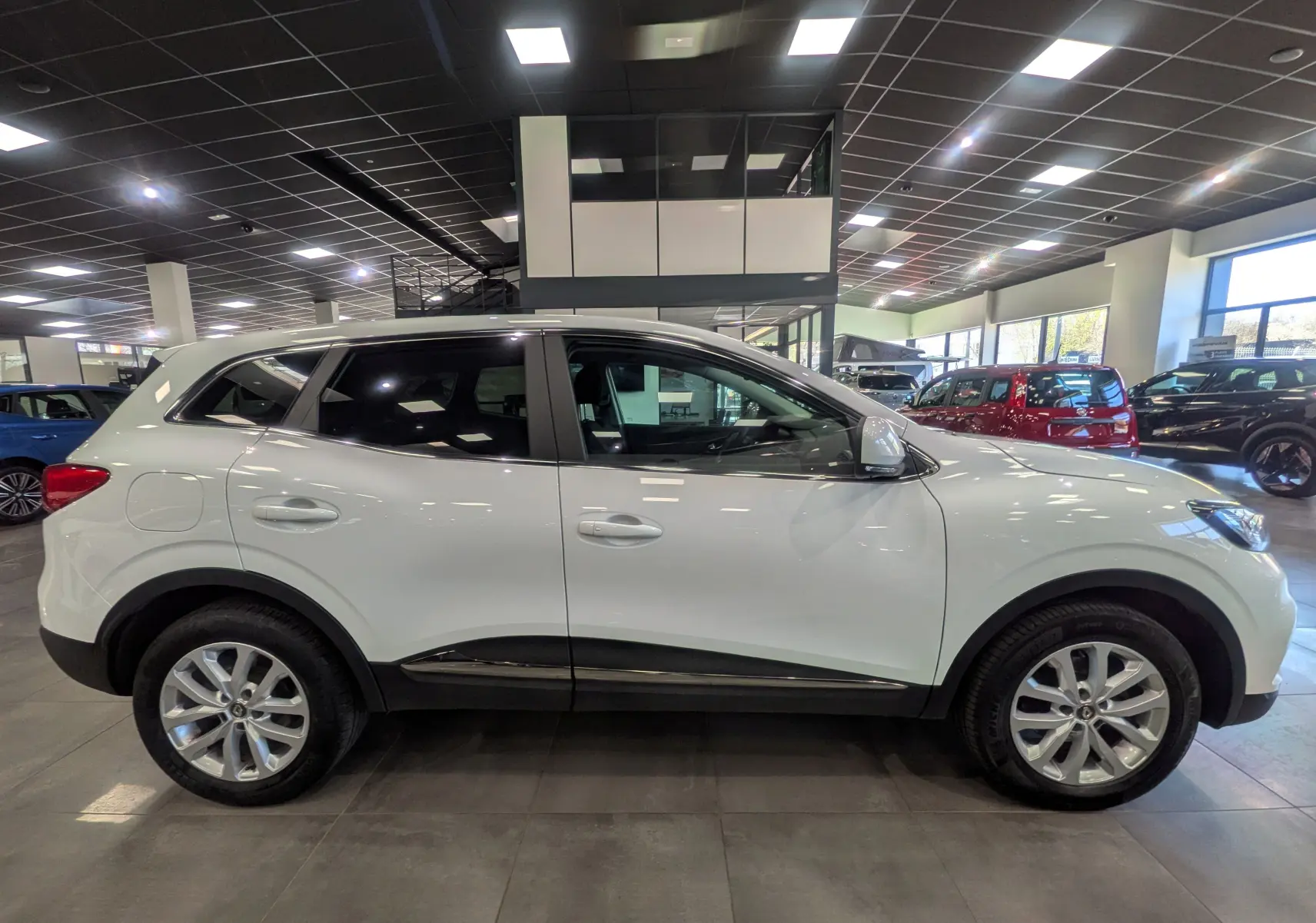 Vue de profil côté gauche d'un Renault Kadjar blanc Glacier 2021 en showroom, avec jantes alliage et vitres teintées.