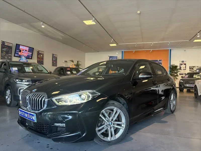 BMW Série 1 noire métal vue 3/4 avant droit en showroom avec jantes alliage et calandre M Sport.