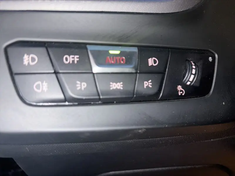 Panneau de commande des phares avec réglage automatique et boutons de feux antibrouillard dans une BMW Série 1 noire.