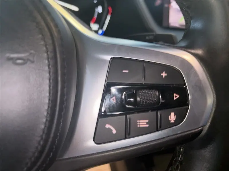 Gros plan sur les commandes multifonctions au volant côté droit d’une BMW Série 1 noire, avec boutons de volume et appel.