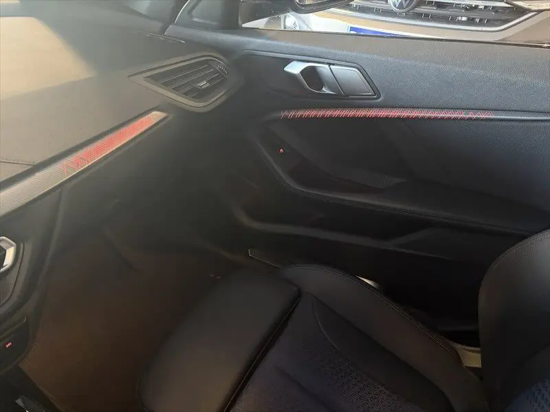 Vue intérieure côté passager de la BMW Série 1 noire, avec détails de la porte et surpiqûres rouges visibles.